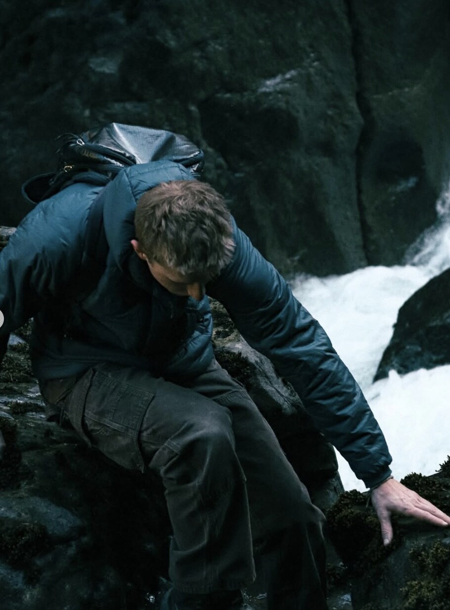 Drake scrambling over rock beside a waterfall